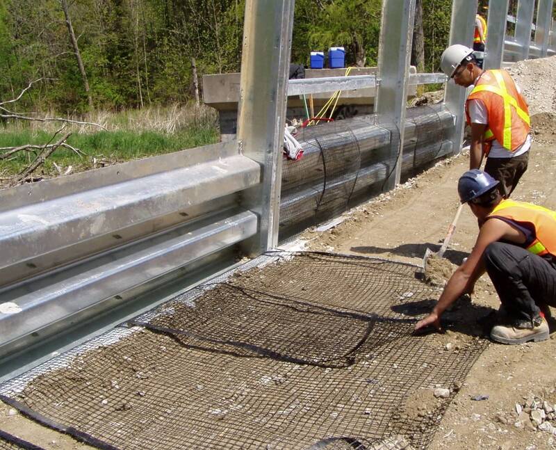 Workers installing Solmax Miragrid XT geogrid at a jobsite
